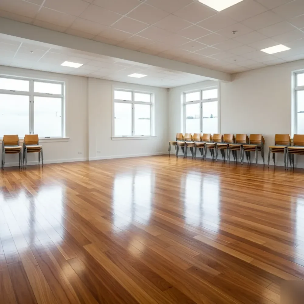 A freshly polished commercial timber floor reflects ceiling light inside a New Zealand office space with stacked chairs.